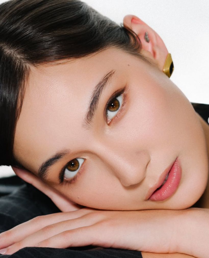 Close-up of a model resting her head on her hands, warm glowing skin, neutral eyeshadow, and a glossy nude lip — a signature soft-glam look from the Jannur portfolio