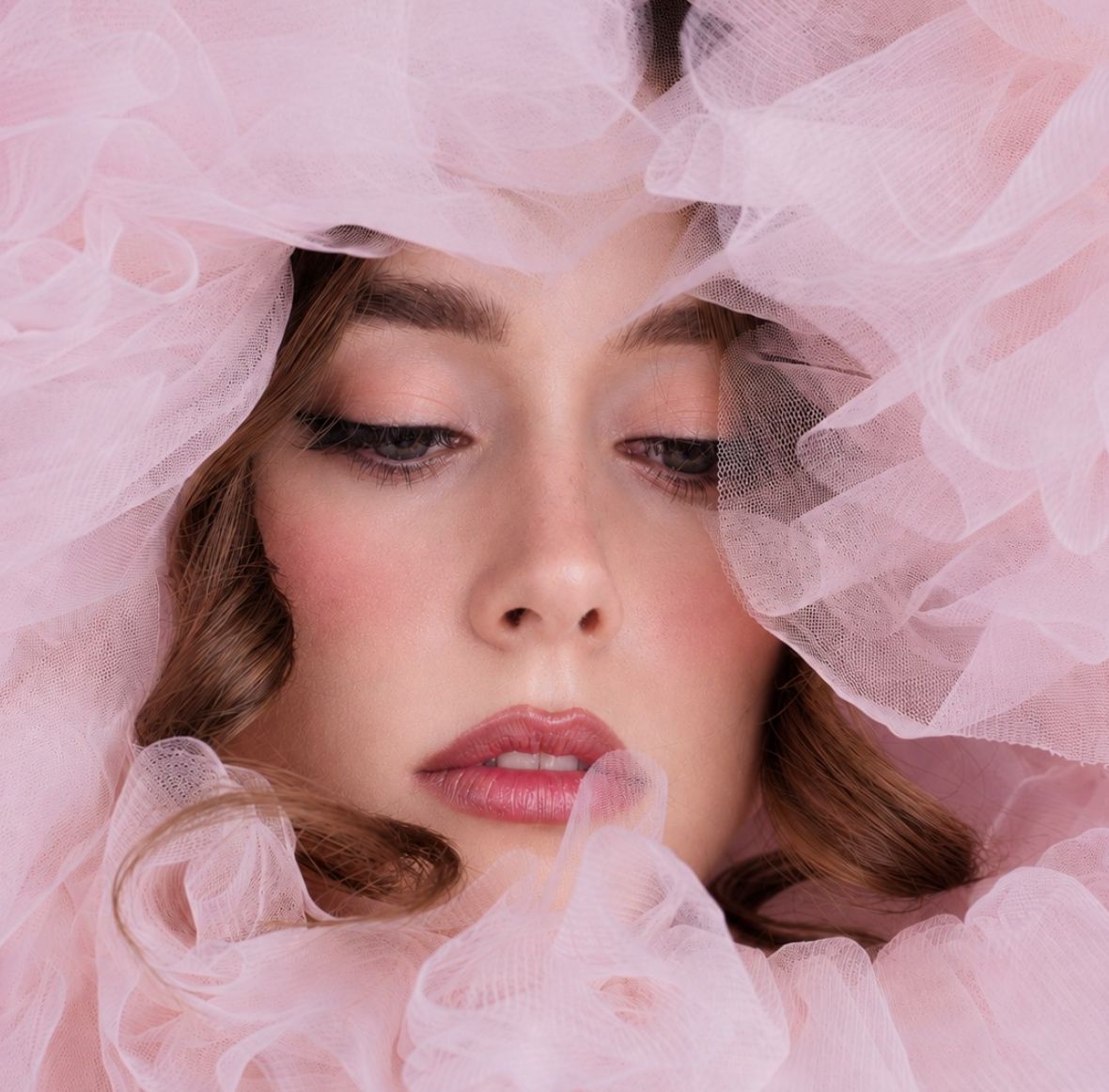 Model's face framed by soft blush-pink tulle, romantic smoky-pink eye makeup and glossy mauve lip