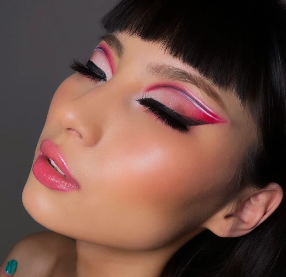 Close-up with blunt bangs and dramatic graphic pink and white winged eyeliner, eyes closed, glossy peach-pink lip