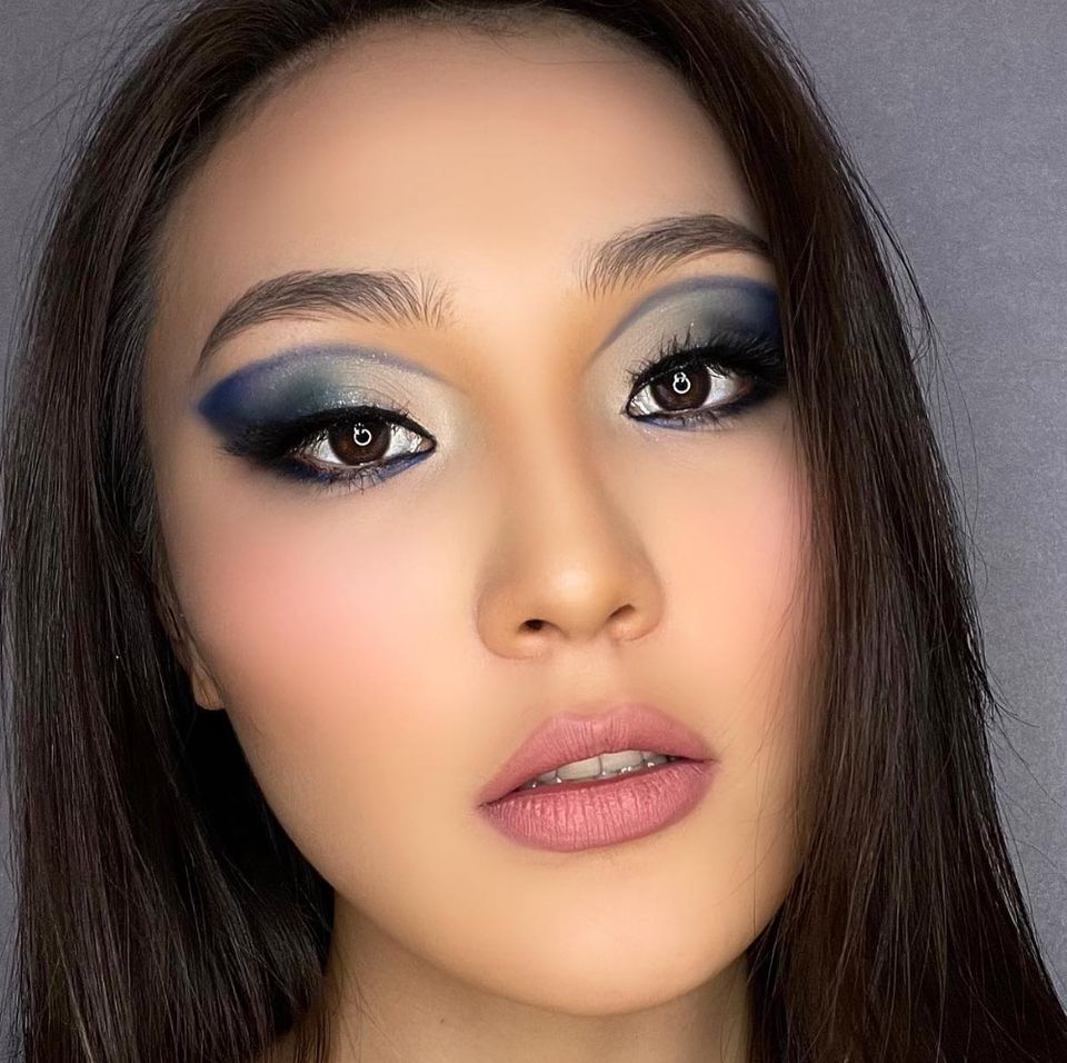 Close-up of a deep navy-blue smoky eyeshadow sharply blended, soft pink blush, and a glossy nude lip