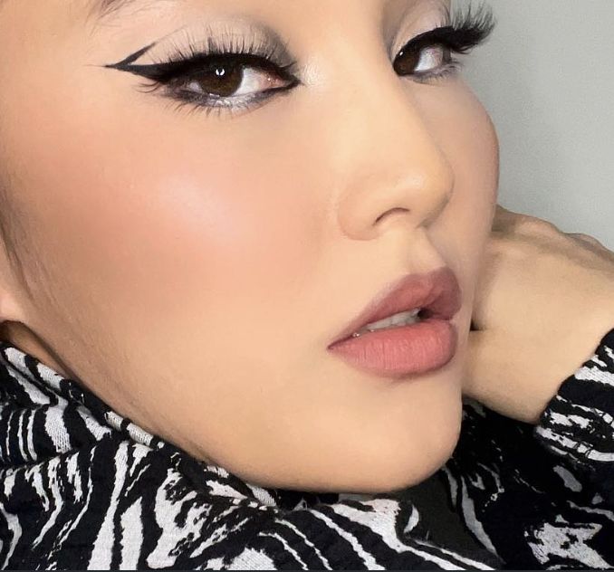 Tight close-up with bold graphic black winged eyeliner using negative space, glowing skin, glossy mauve lip, and an animal-print top